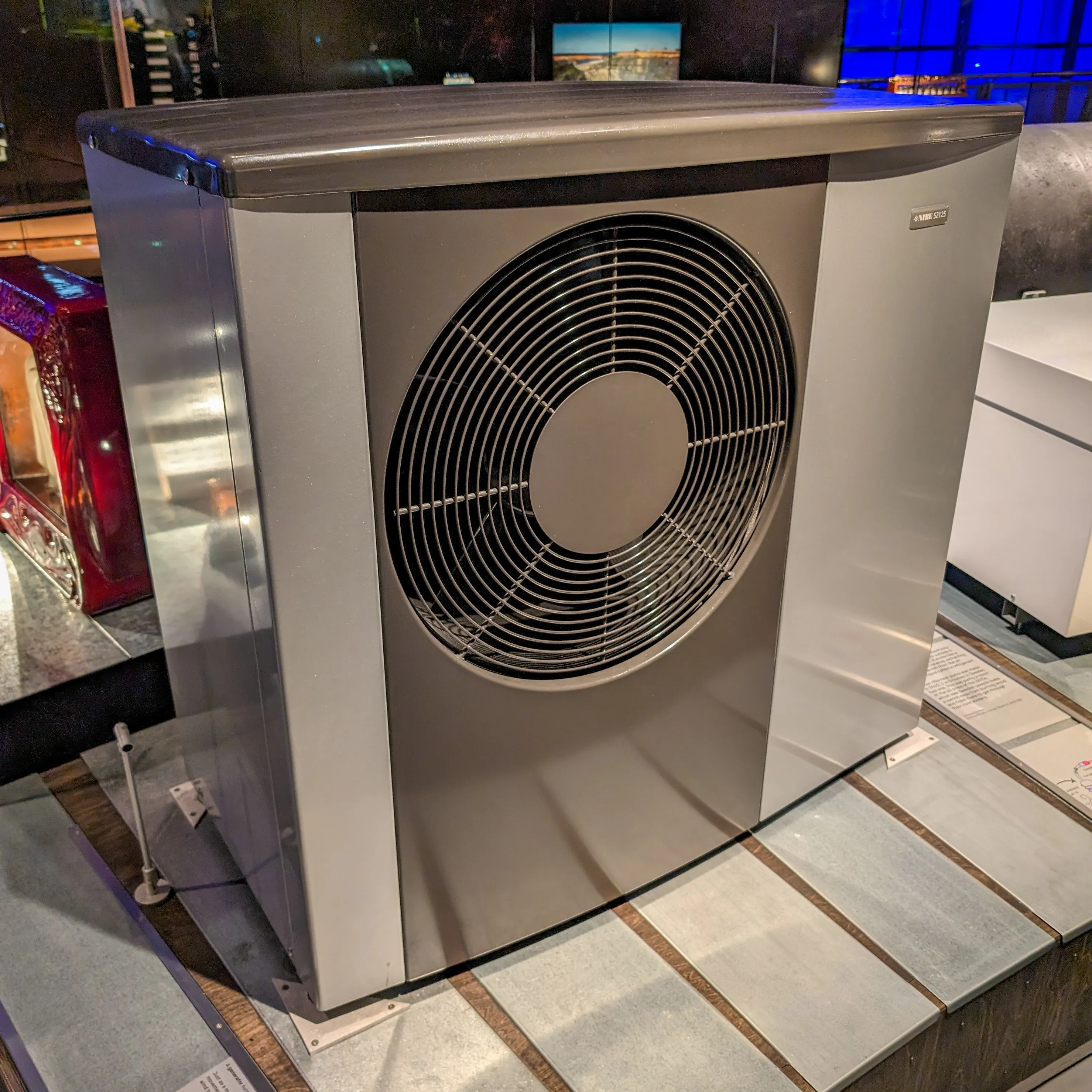 A modern grey air-source heat pump unit with a large front fan on a low plinth — SCOP measures this kind of unit's seasonal efficiency across the full range of UK heating conditions.