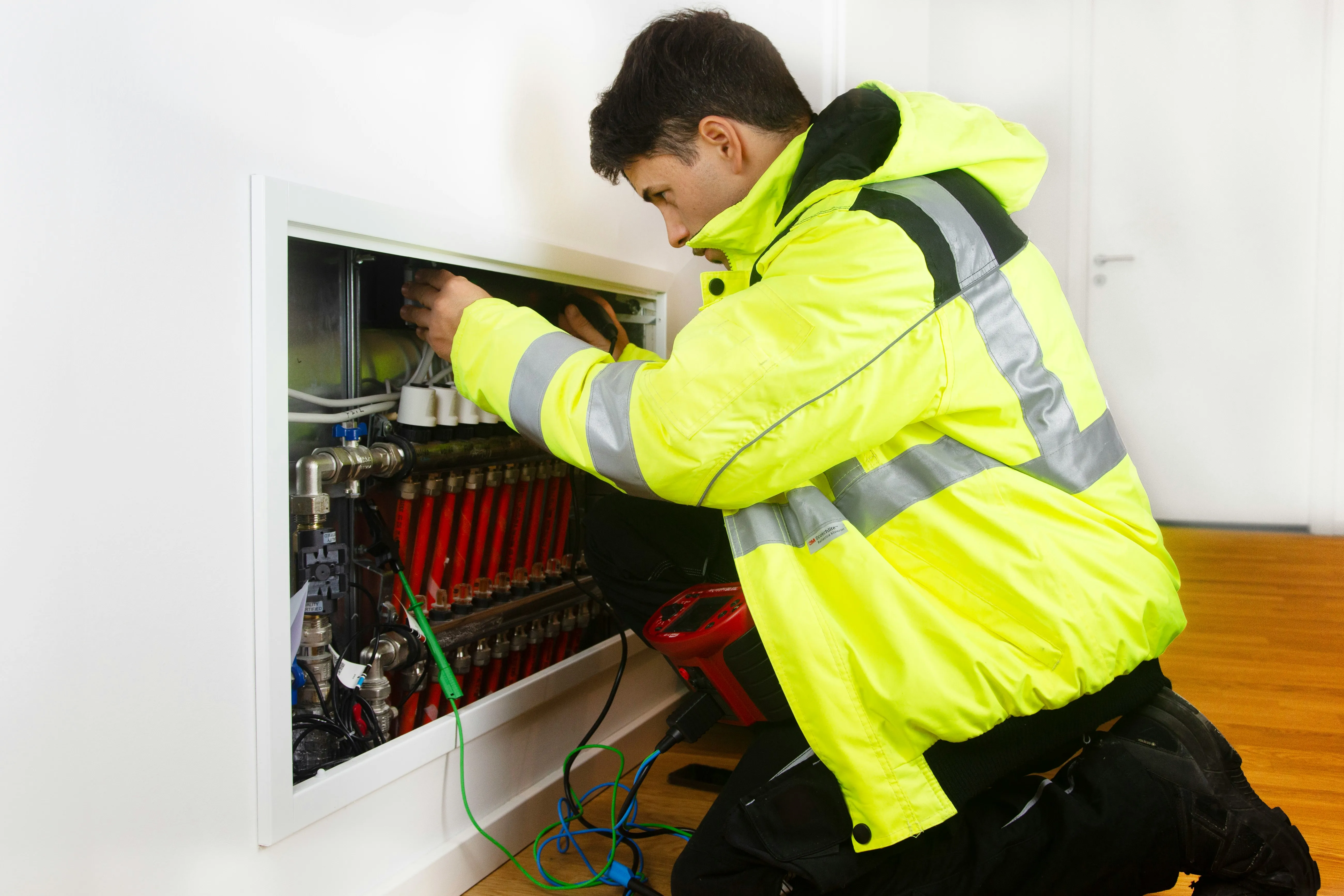 Engineer working on a heating-system distribution manifold during a heat pump maintenance visit